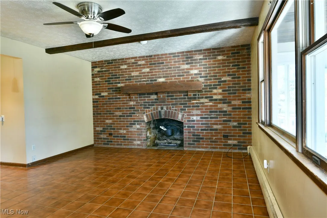 Unfurnished living room with beam ceiling, a baseboard radiator, a textured ceiling, tile patterned floors, and brick wall