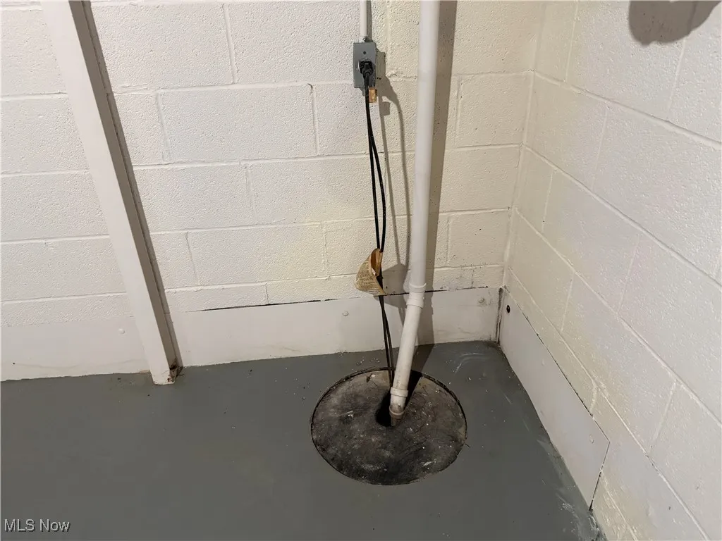 Basement view of concrete block wall, finished concrete flooring, and drainage system