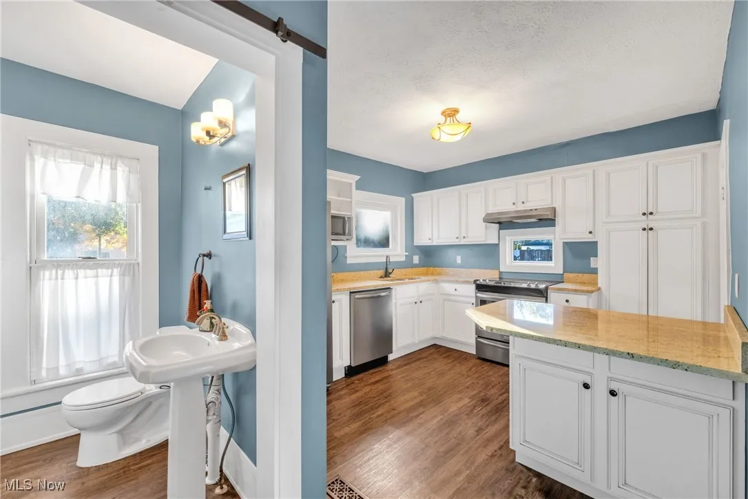 Kitchen featuring healthy amount of natural light, appliances with stainless steel finishes, light stone countertops, white cabinets, and a textured ceiling