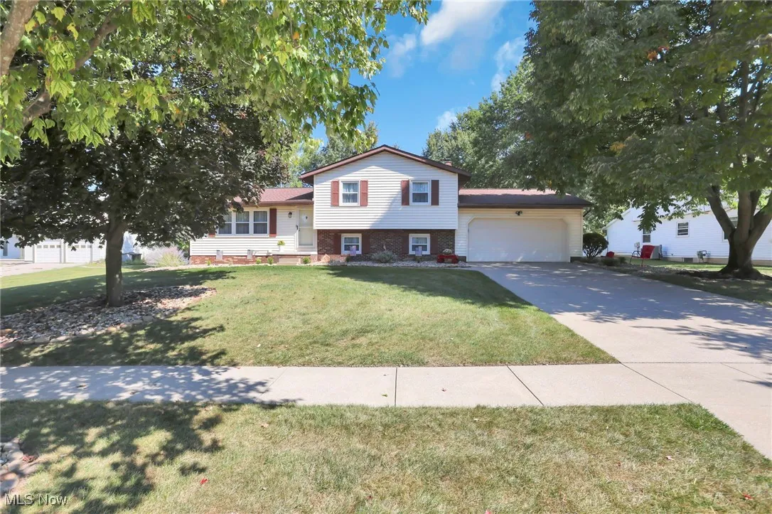 Split level home with a front yard, an attached garage, driveway, and brick siding