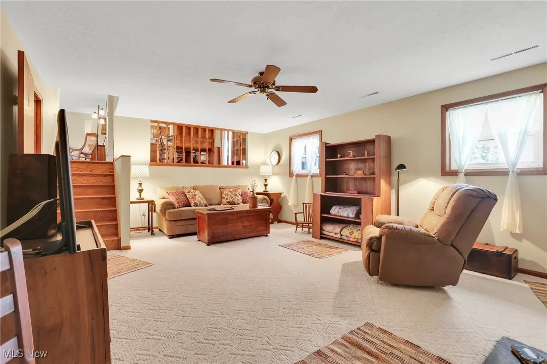 Living area featuring carpet, ceiling fan, and stairs