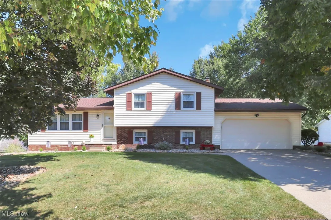 Tri-level home featuring an attached garage, concrete driveway, a front lawn, and brick siding