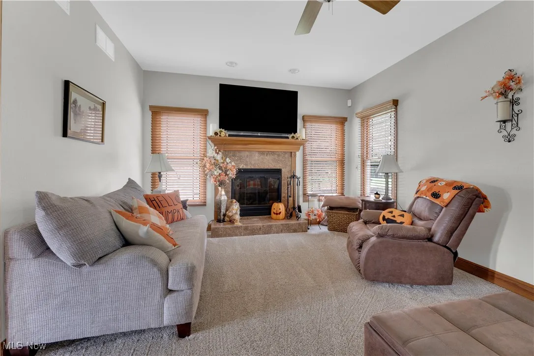 Carpeted living room featuring a tiled fireplace and a ceiling fan