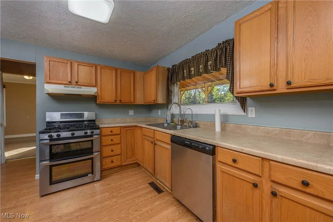 Kitchen featuring stainless steel appliances, a textured ceiling, light countertops, light wood-type flooring, and under cabinet range hood