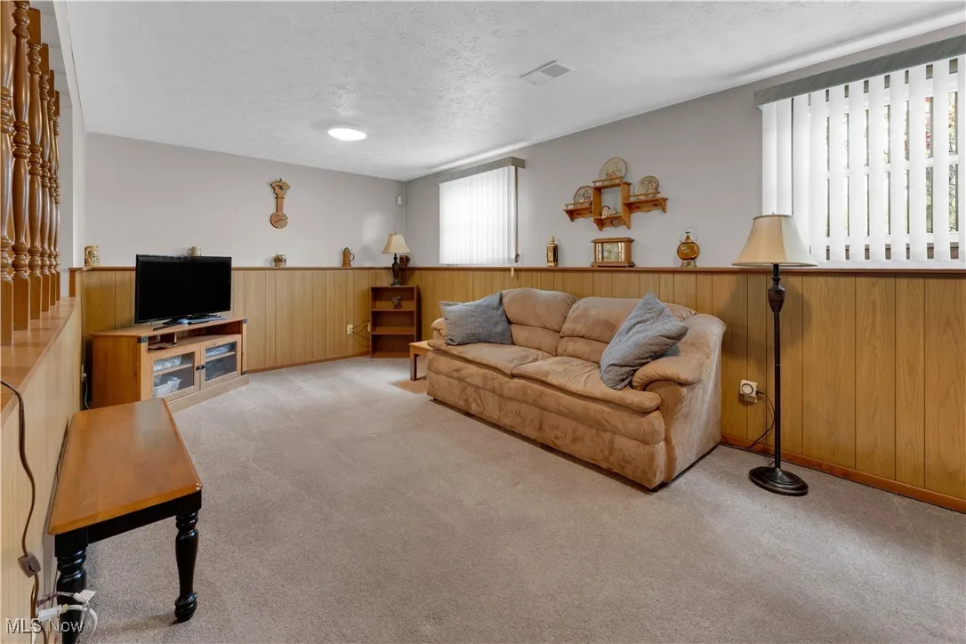 Living room with a textured ceiling, wood walls, carpet floors, and wainscoting