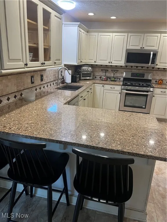 Kitchen with dark stone counters, a kitchen bar, range, a textured ceiling, and a peninsula