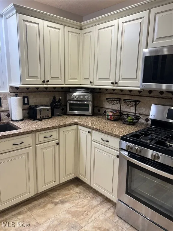 Kitchen featuring range, stainless steel microwave, decorative backsplash, and light stone countertops