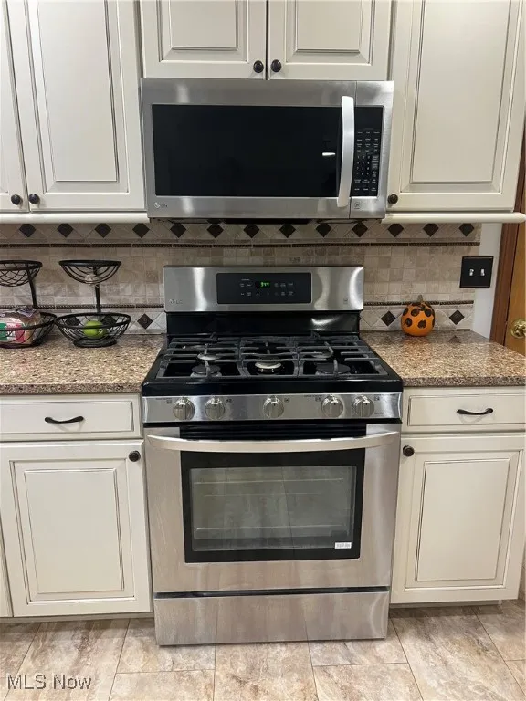 Kitchen with stainless steel range with gas cooktop, white microwave, light stone counters, decorative backsplash, and white cabinets