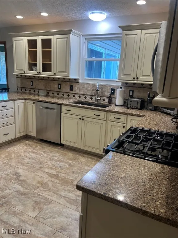 Kitchen with backsplash, dark stone counters, dishwasher, stove, and a textured ceiling