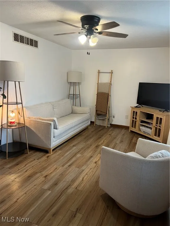 Living area with wood finished floors, a ceiling fan, and a textured ceiling