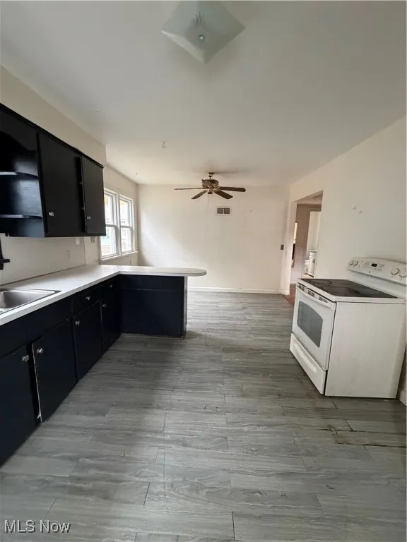 Kitchen featuring dark cabinets, a peninsula, stove, light countertops, and light wood finished floors