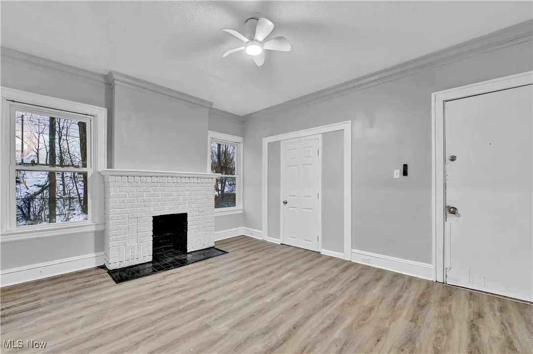 Unfurnished living room with crown molding, a brick fireplace, light wood-style floors, and a ceiling fan