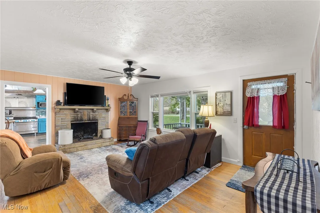 Living area featuring hardwood / wood-style flooring, a stone fireplace, ceiling fan, wooden walls, and a textured ceiling