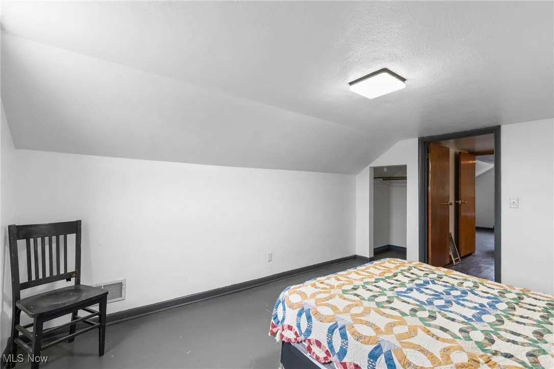 Bedroom with vaulted ceiling, a closet, a textured ceiling, and concrete flooring