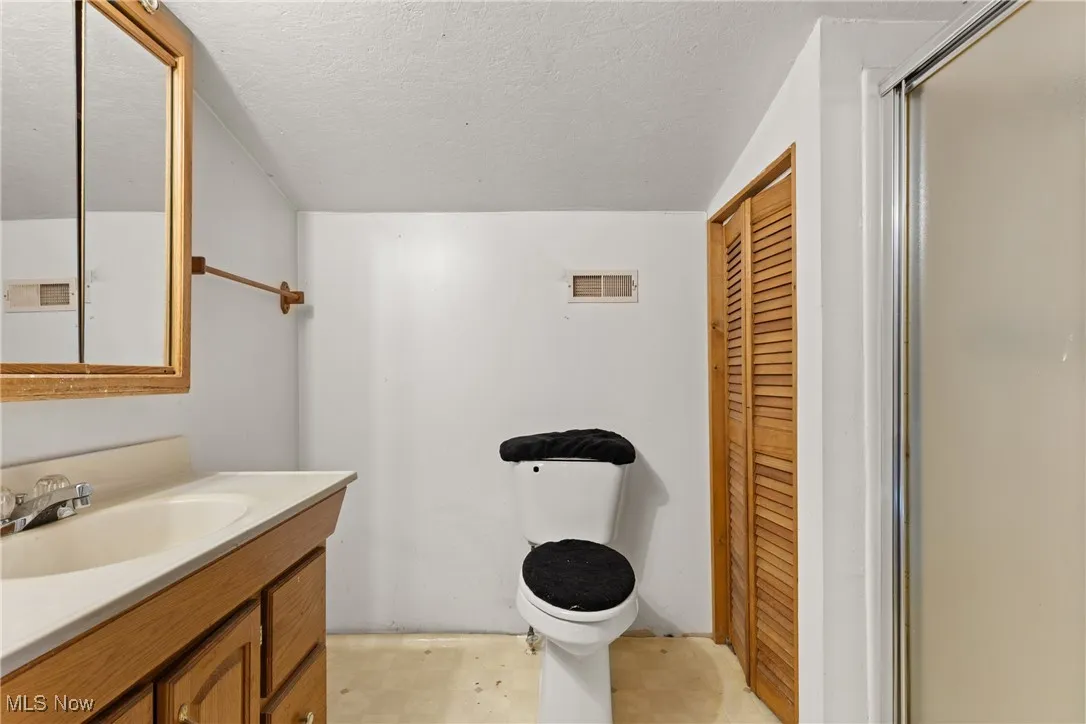 Full bathroom with a textured ceiling, a closet, vanity, and a shower with door