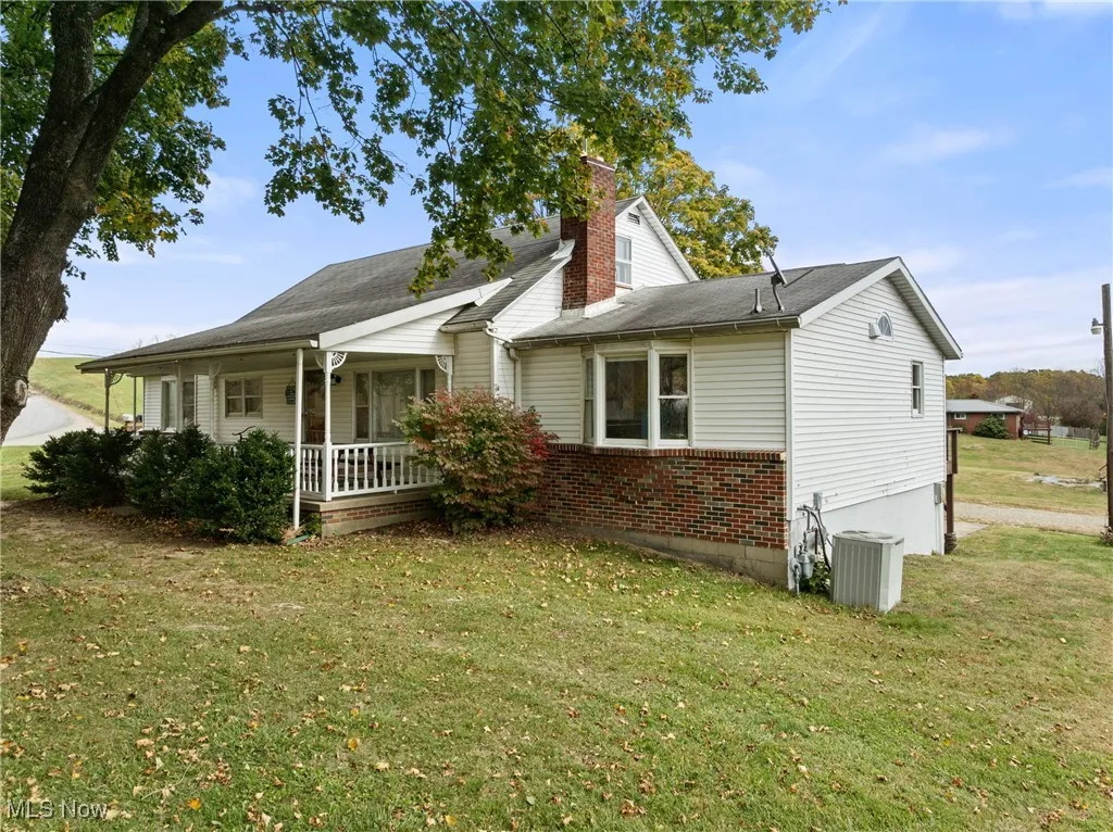 View of property exterior with a lawn, a chimney, brick siding, and a porch