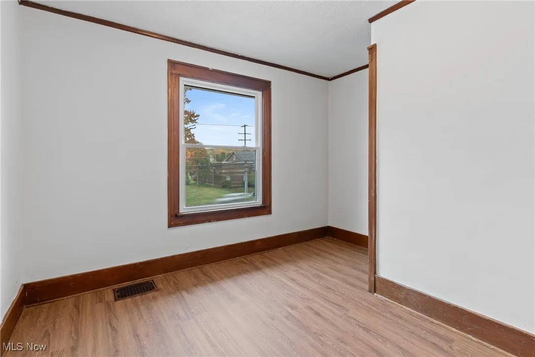 Empty room with crown molding and light wood finished floors