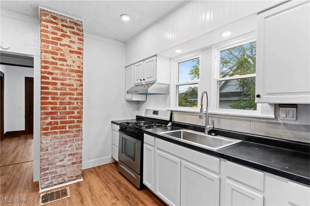 Kitchen featuring stainless steel gas range oven, dark countertops, light wood finished floors, a textured ceiling, and white cabinetry