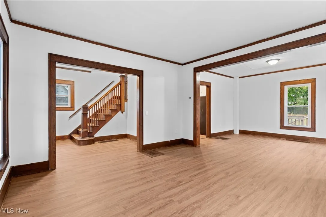 Unfurnished living room featuring crown molding, light wood finished floors, and stairs