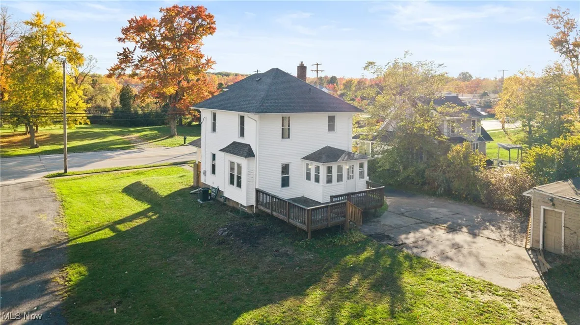 View of side of property with a yard, a deck, roof with shingles, and a patio area
