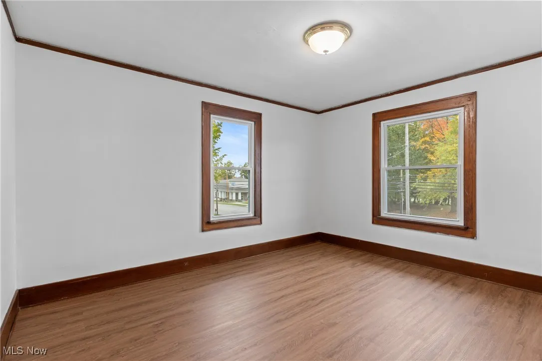 Empty room featuring wood finished floors, crown molding, and healthy amount of natural light