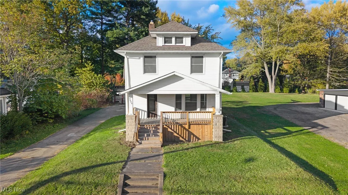 Traditional style home featuring a front yard, a chimney, roof with shingles, covered porch, and driveway