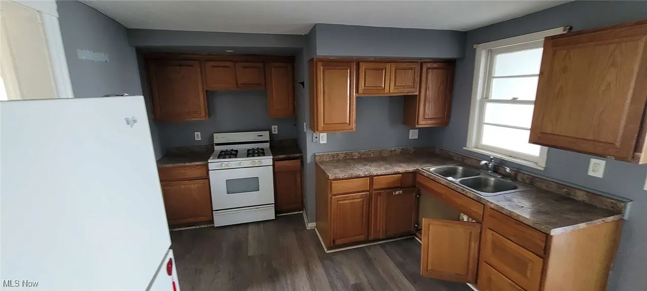 Kitchen with white appliances, brown cabinets, and dark wood-style floors