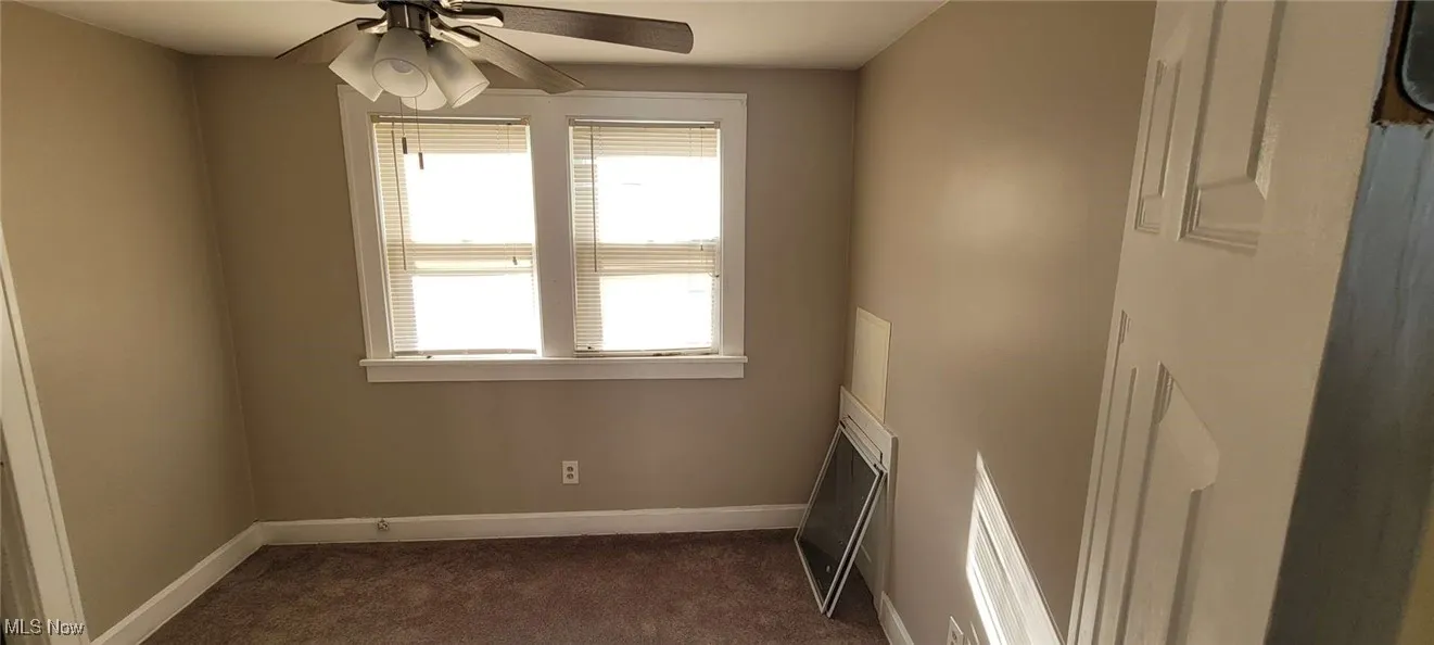 Empty room with dark colored carpet and ceiling fan