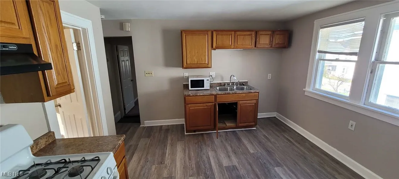 Kitchen with white appliances, dark countertops, dark wood-style flooring, brown cabinetry, and under cabinet range hood