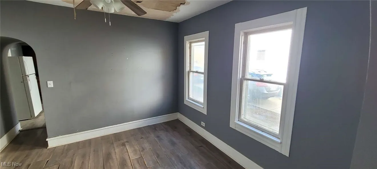 Unfurnished room with dark wood-type flooring, arched walkways, and ceiling fan