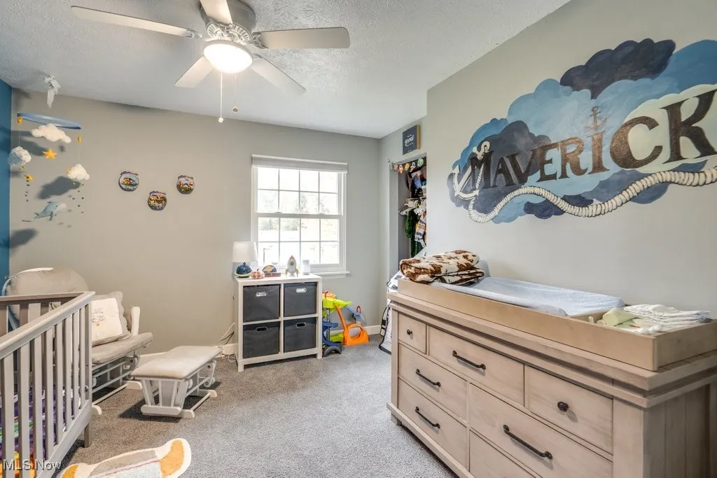 Bedroom with a textured ceiling, a crib, light carpet, and a ceiling fan