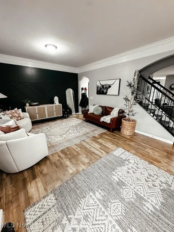 Living area with arched walkways, stairway, ornamental molding, and wood finished floors