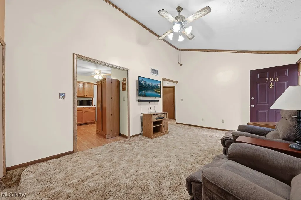 Living area featuring ornamental molding, ceiling fan, light colored carpet, and high vaulted ceiling