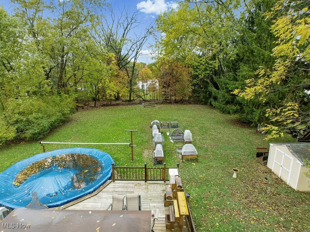 View of green lawn featuring a wooden deck and view of scattered trees