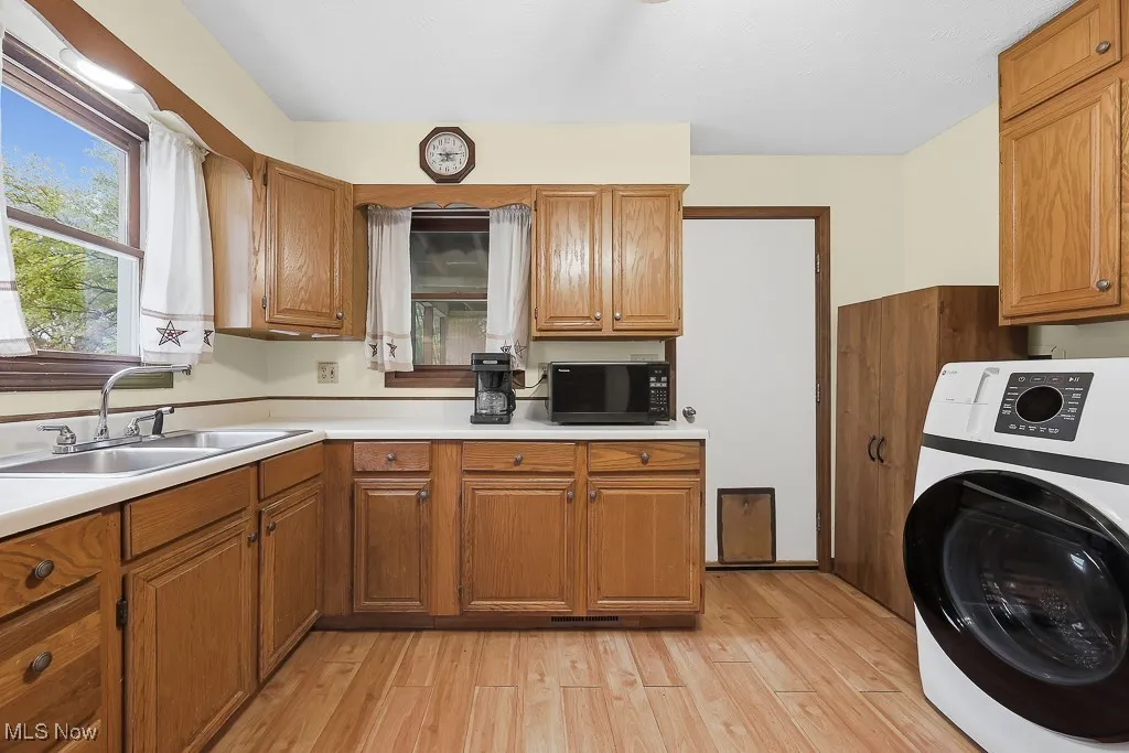 Kitchen with washer / dryer, brown cabinets, light wood-type flooring, and black microwave