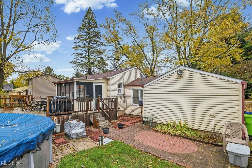 Rear view of house featuring a patio, a wooden deck, a sunroom, roof with shingles, and outdoor dining space