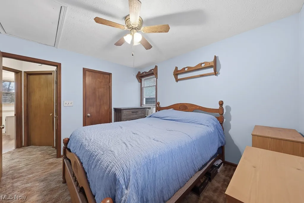 Bedroom with ceiling fan, a textured ceiling, multiple closets, and dark colored carpet