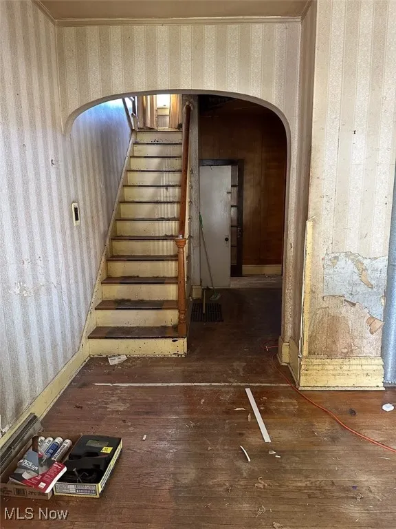 Stairway featuring arched walkways, wallpapered walls, and hardwood / wood-style flooring