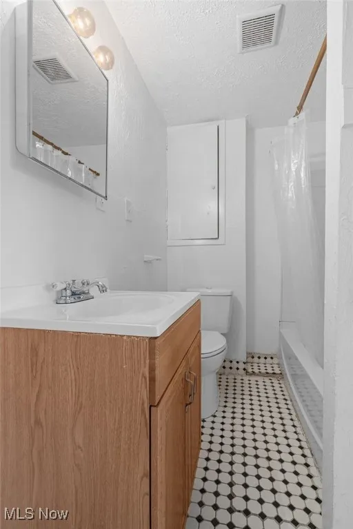 Bathroom with a textured ceiling, vanity, and shower / tub combo with curtain