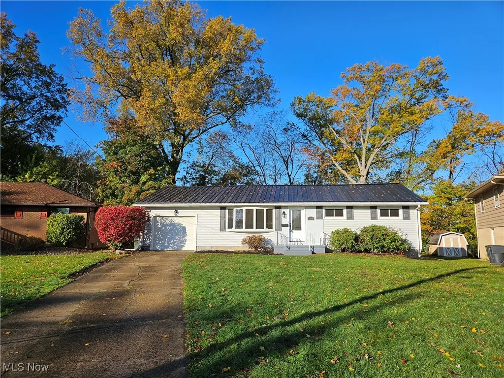 Single story home featuring concrete driveway, a front yard, a garage, and a metal roof