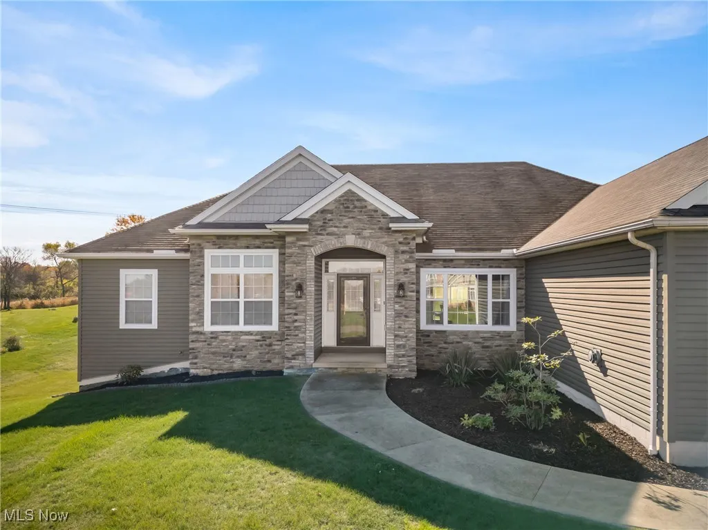 View of front facade with a front yard, stone siding, and a shingled roof