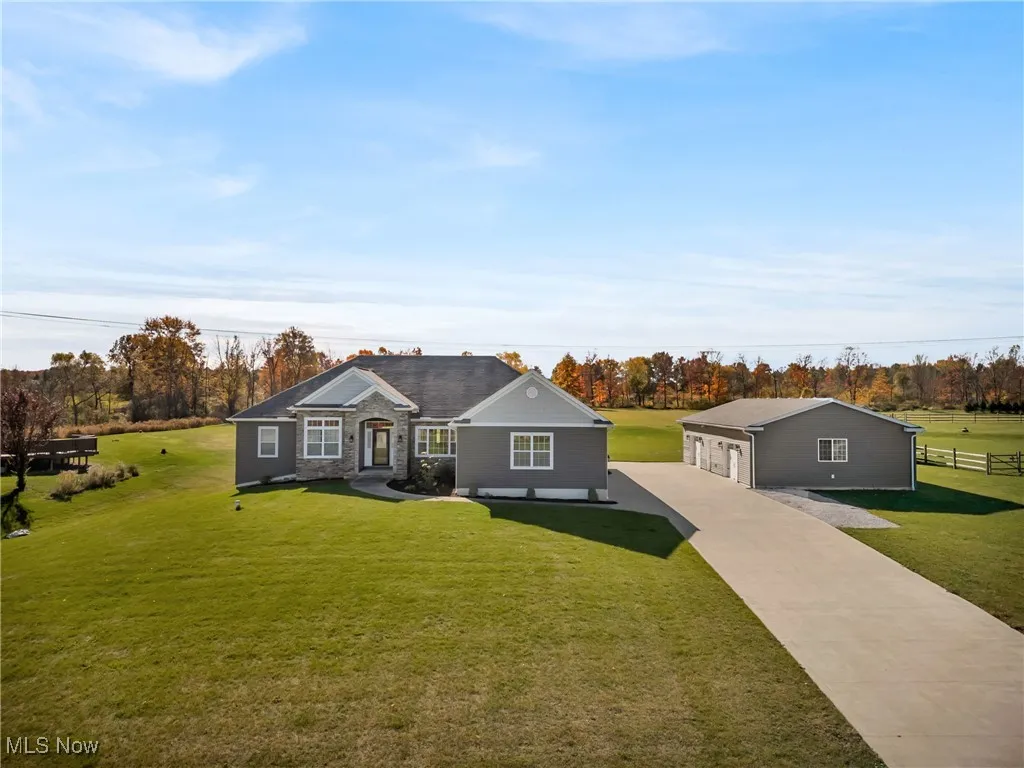 View of front of property with a front yard, concrete driveway, a garage, stone siding, and an outbuilding