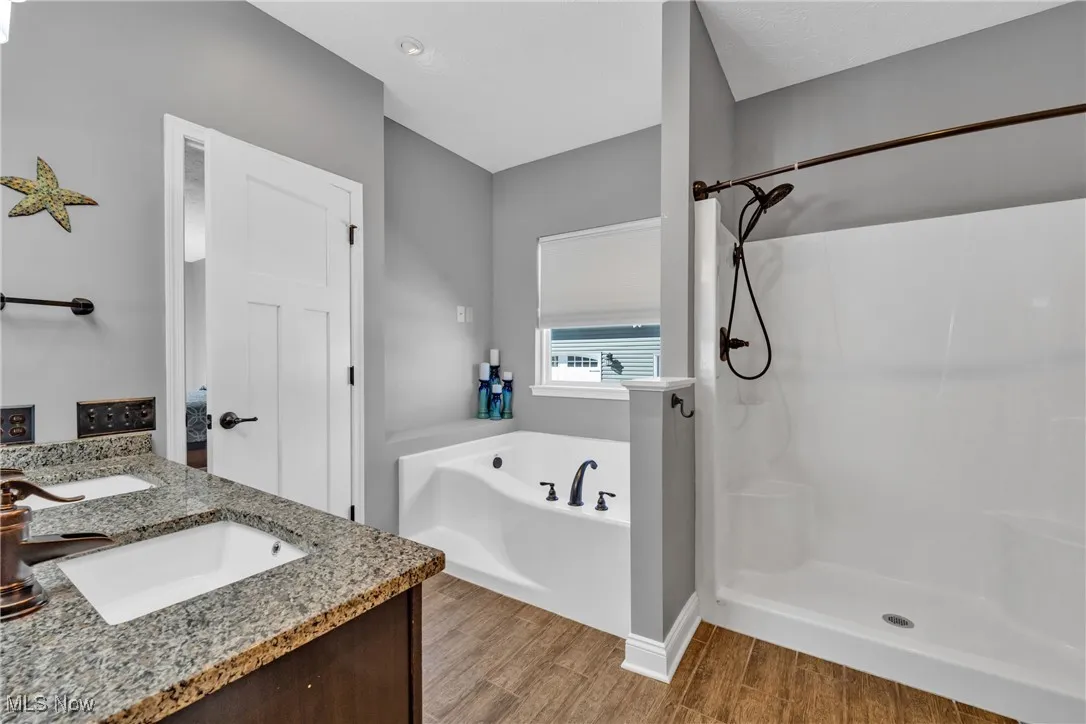 Bathroom featuring double vanity, light wood finished floors, a bath, and a stall shower