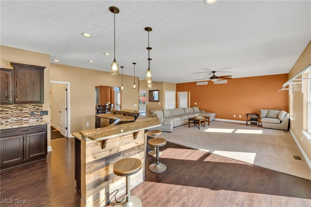 Kitchen featuring light stone counters, dark brown cabinetry, dark wood finished floors, a breakfast bar, and open floor plan