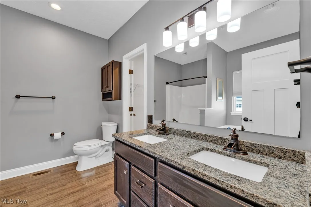 Full bath featuring double vanity, light wood-style floors, and a shower