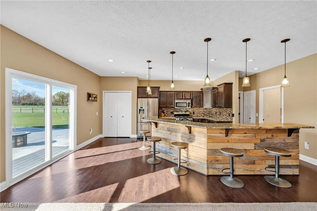 Kitchen with dark brown cabinets, light stone counters, backsplash, appliances with stainless steel finishes, and dark wood-style floors