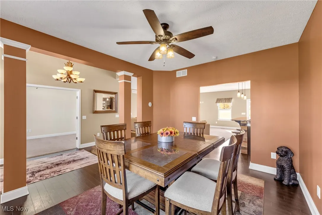 Dining space with a chandelier, dark wood-style floors, ornate columns, a ceiling fan, and a textured ceiling