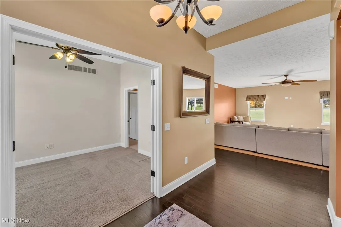 Unfurnished living room featuring ceiling fan, a textured ceiling, dark wood-type flooring, and a chandelier