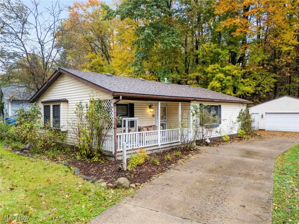 Ranch-style house featuring an outbuilding, a porch, a detached garage, a front lawn, and a shingled roof
