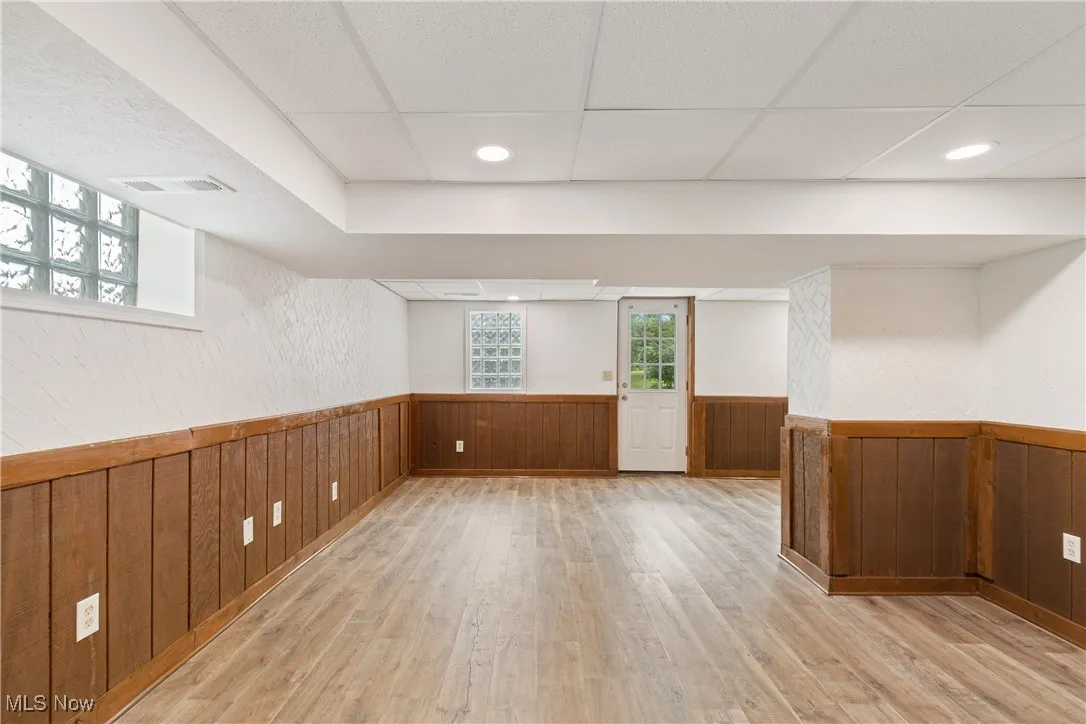 Basement featuring light wood-type flooring, wood walls, a drop ceiling, wainscoting, and recessed lighting